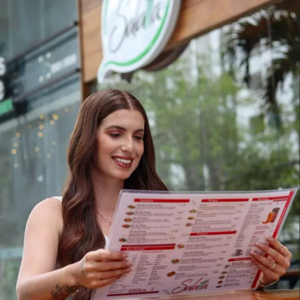 Cliente sorrindo enquanto lê o cardápio do Salatta na área externa do restaurante